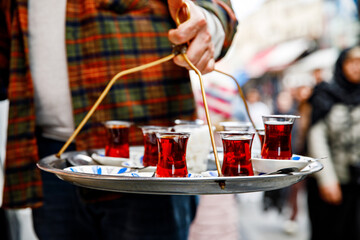 Turkish tea in traditional glass mugs on a metal tray. Street vendor selling hot tea in Istanbul, Turkey, Grand Bazaar.