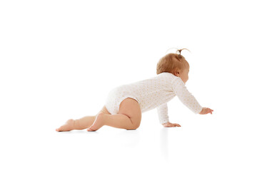 Cute little baby girl crawling on floor in comfortable clothes and looking with curiosity isolated on white background. Playful happy kid. Concept of childhood, care, health, well-being, parenthood