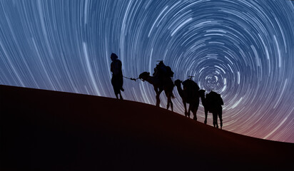 Camel caravan in the desert - Long exposure photo of night sky star trail over the sand dunes of...