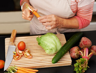 Senior woman or closeup with salad in kitchen and cutting, tomato and carrots for diet. Female chef and zoom with healthy vegetables for nutrition, peeling green lettuce with onion in retirement home
