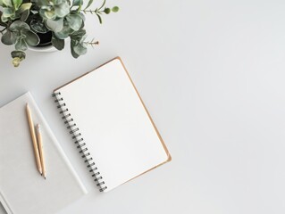 A white notebook sits on a table next to a pencil and a potted plant