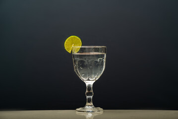a glass cup with clear water and a lemon on the rim. Isolated on gray background.
