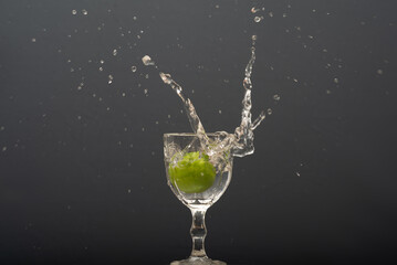 Lemon falling into a glass of transparent water causing splashes upwards. Isolated on gray background.
