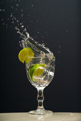 Lemon falling into a glass of transparent water causing splashes upwards. Isolated on gray background.