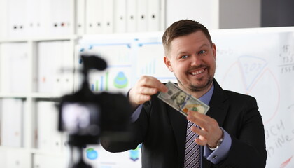 Male in suit and tie dollar banknote making promo videoblog or photo concept in office camcorder to tripod portrait