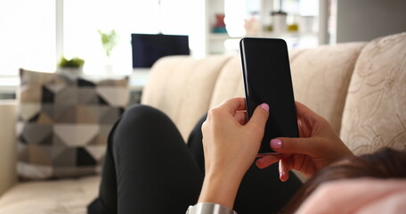 Young beautiful woman holds smartphone in hand using at home costs about sofa. Verifies internal information its financial advertising freedom makes money level transfer to contractor concept