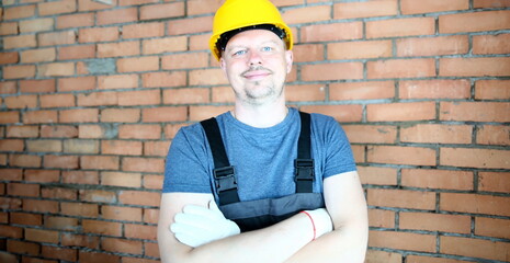 Portrait of laughing male looking at camera joyfully. Self-confident builder posing in protective hardhat prevent any trauma and injury. Constructor standing at concrete wall. Building concept