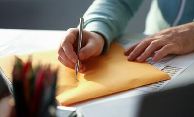 Male hand holding silver pen. Fill in address on yellow envelope of mail correspondence for application hiring concept