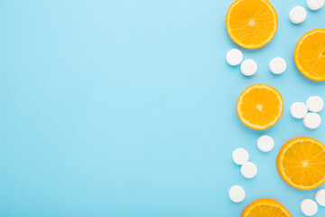 White pills of c vitamin and cut slices of fresh orange fruit on light blue table background. Pastel color. Closeup. Empty place for text. Top down view. - 783033212