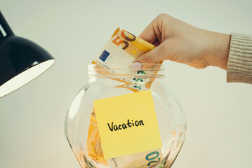 Euro banknote in hand of a person, putting it into the glass jar, toned close up photo. Vacation...