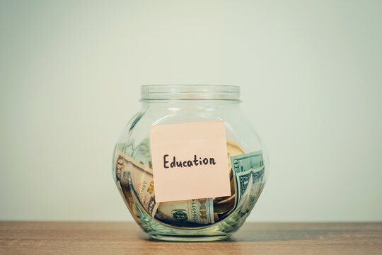 A jar with dollar banknotes and sticker with word "education" on it, stands on the table, close up, toned photo. Concept of saving money for education, investment into the knowledges