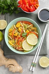 Stir-fry. Delicious cooked noodles with chicken and vegetables in bowl served on gray textured table, flat lay