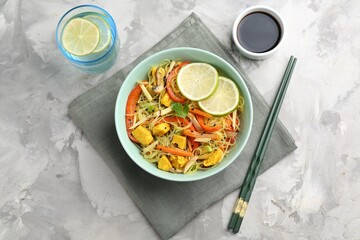 Stir-fry. Delicious cooked noodles with chicken and vegetables in bowl served on gray textured table, flat lay