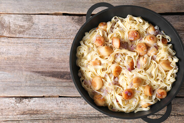 Delicious scallop pasta with onion in pan on wooden table, top view. Space for text
