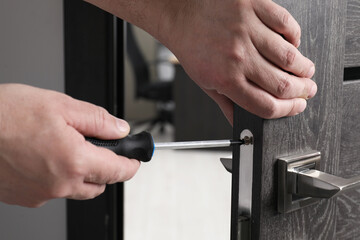 Handyman with screwdriver repairing door handle indoors, closeup