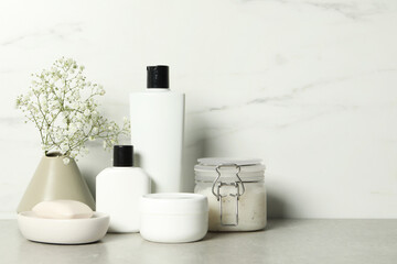 Bath accessories. Personal care products and gypsophila flowers in vase on gray table near white marble wall, space for text
