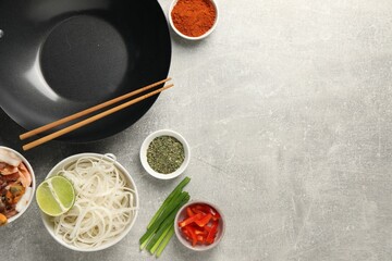 Flat lay composition with black wok, spices and products on grey textured table. Space for text