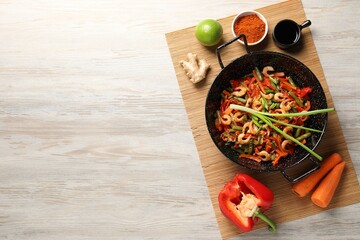 Shrimp stir fry with vegetables in wok and ingredients on wooden table, flat lay. Space for text