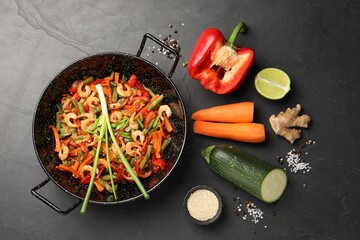 Shrimp stir fry with vegetables in wok and ingredients on black table, flat lay