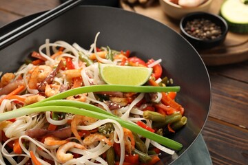 Shrimp stir fry with noodles and vegetables in wok on wooden table, closeup