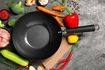 Empty iron wok surrounded by raw ingredients on grey table, flat lay