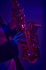 Cropped photo of talented solo player performing on saxophone in vibrant pink neon light against...