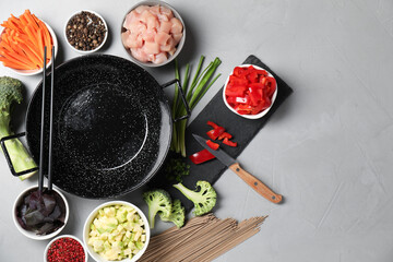 Wok pan, noodles, chicken and other products on light grey table, flat lay. Space for text