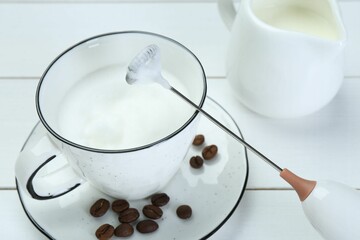 Mini mixer (milk frother), whipped milk and coffee beans on white wooden table, closeup