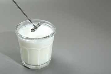 Mini mixer (milk frother) and whipped milk in glass on grey background. Space for text