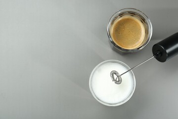 Mini mixer (milk frother), whipped milk and coffee in glasses on grey background, flat lay. Space for text