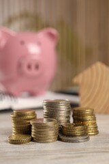 House model, stacked coins and piggy bank on wooden table, selective focus