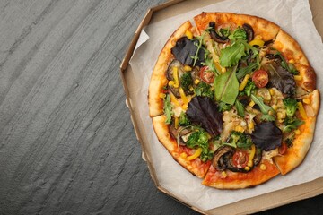 Delicious vegetarian pizza with mushrooms, vegetables and greens in box on black table, top view. Space for text