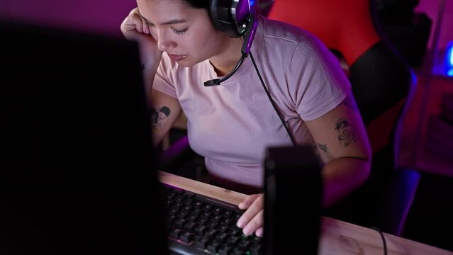 Young hispanic woman gaming indoors at night in a dark room, wearing headphones, focused, and beautiful.