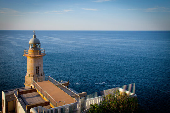 This vibrant image captures a coastal lighthouse standing tall at the edge of a cliff, overlooking the vast sea under clear skies