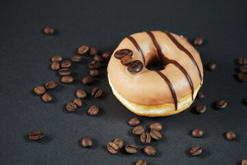 Caramel donut with coffee decor next to scattered coffee beans on a dark background