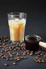 Glass of Frappuccino with ice and glass coffee scoop on dark background