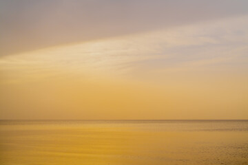 Lovely sunset evening across cloudy sea with no waves at calm weather without wind
