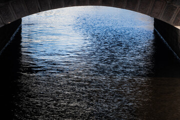 Under the bridge river bank water flow surface close up in city