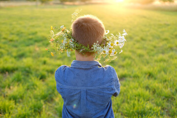 happy boy in wreath, floral crown on green sunlit meadow rear view, seen from behind, beauty nature...