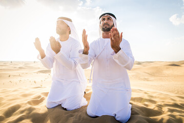 Two arab men wearing traditional emirati clothing in the desert of Dubai - Middle-eastern adult males portrait praying - obrazy, fototapety, plakaty