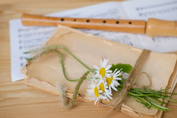 cozy scene with daisies flowers on rustic paper texture, wooden flute, sheet music, German...