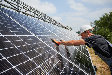 Worker mounting photovoltaic solar panel system outdoors. Man engineer placing solar module on metal rails, wearing construction helmets and work gloves. Renewable and ecological energy.