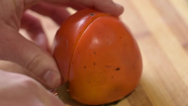 Cutting persimmon in half on wooden table. Eating tasty and juicy date-plum