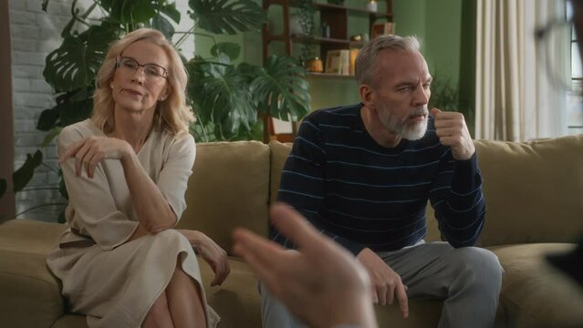 adult couple sitting on couch in psychologist office . middle age man and woman do not talk to each other during family therapy. angry husband does not look on annoyed wife due to misunderstanding
