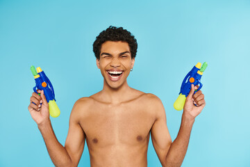 positive handsome african american man posing with two water guns and smiling at camera happily