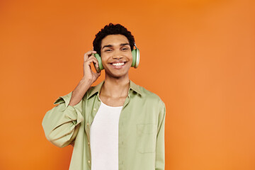 merry trendy african american man in casual clothes with headphones and smiling at camera happily