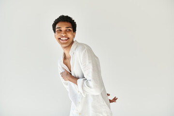 happy alluring african american male model in white linen attire looking away on beige backdrop
