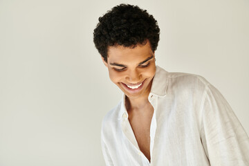 positive alluring african american male model in white linen attire looking away on beige backdrop