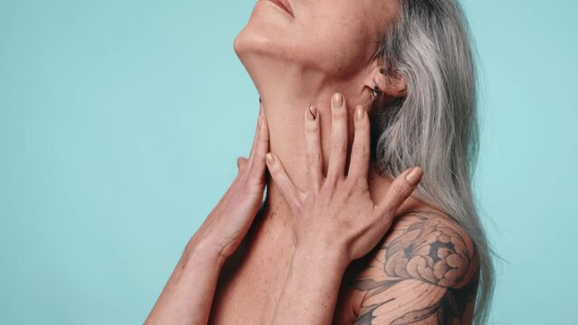 An elderly woman appreciating her smooth skin, touching her neck and showcasing self-care and confidence on a colored background.