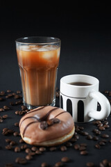 Caramel donut with coffee decoration next to a glass of iced frappuccino with a cup of black coffee on a dark background